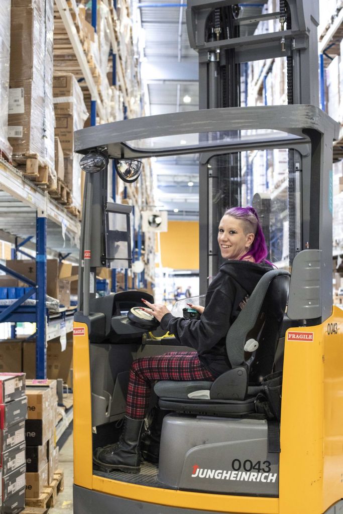 Femme souriant sur un chariot élévateur dans un centre de logistique